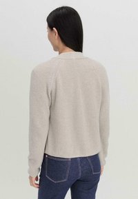 Lichtbeige geribde gebreide trui met een cropped ontwerp, raglanmouwen en een ronde halslijn, in combinatie met donkerblauwe jeans.