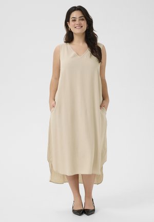 Beige sleeveless dress with a V-neck, side pockets, and an asymmetrical hemline. Made of lightweight fabric with a smooth texture.