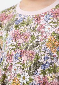 Gros plan sur un vêtement avec un motif floral comprenant des fleurs roses, jaunes et bleues, des feuilles vertes et de petits papillons sur un tissu clair.