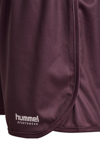 Vinröda sportshorts av lätt tyg med en slät textur, med en vit "hummel"-logotyp på nedre vänstra sidan.