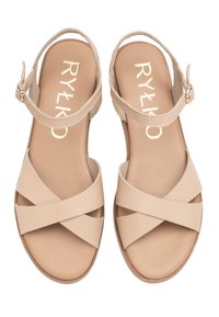 Beżowe sandały na krzyż z gładkiej skóry, z teksturowanym paskiem na kostce i zapięciem na klamrę. Wyściółka amortyzująca i płaska podeszwa.