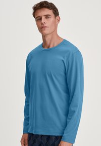 Long-sleeve shirt in solid blue cotton fabric, featuring a round neckline and relaxed fit. The design is simple with no additional patterns or accents.