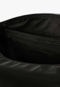 Interno di una borsa nera con zip, caratterizzato da una texture liscia, con una piccola tasca con zip e un'etichetta in pelle impressa con la scritta "SCALPERS."