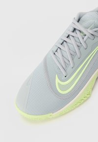 Szare buty sportowe z teksturowanym wierzchem, neonowożółtymi akcentami i gumową podeszwą. Posiadają sznurówki i wyraźne logo na boku.