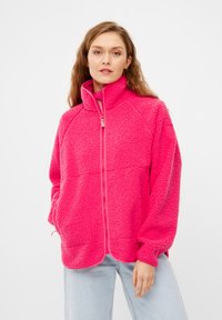Giacca in pile di un vivace colore rosa con colletto alto e zip a tutta lunghezza. Presenta maniche raglan e una superficie morbida e testurizzata. Due tasche laterali.