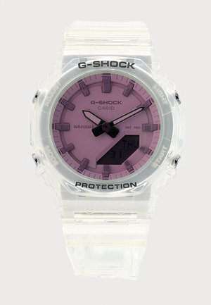 Przezroczysty zegarek Casio G-Shock na nadgarstek z fioletową tarczą analogowo-cyfrową, czarnymi wskazówkami oraz przezroczystym paskiem i kopertą pokazującymi datę i dzień.