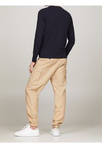 Beige cargo pants with elastic cuffs, featuring side pockets and a flat front. Paired with a fitted navy long-sleeve shirt and white sneakers.