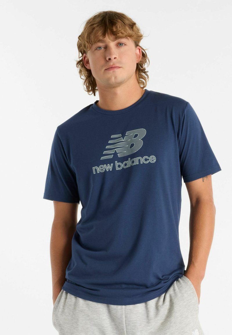 Camiseta de manga corta azul marino en tela suave, con un logo de New Balance en gris claro en el centro, combinada con pantalones cortos deportivos grises.
