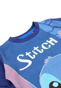 T-shirt en coton bleu à manches courtes, avec une impression de personnage et le texte "Stitch" en blanc. Col rond avec une bordure bleu foncé.