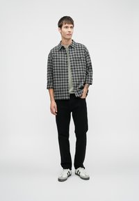 Grå og sort ternet skjorte over en grøn t-shirt, parret med sorte bukser og hvide sneakers. Korte ærmer, afslappet design, minimal dekoration.