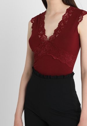 Bordeauxroter Body mit Spitzenbesatz und tiefem V-Ausschnitt, mit kurzen Ärmeln und glatter Textur, kombiniert mit schwarzen, hoch taillierten Hosen.