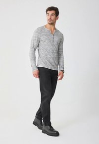 Graues Langarm-Henley-Shirt mit geknöpftem Kragen, kombiniert mit schlanken schwarzen Hosen und schwarzen Schnürschuhen. Glatter Stoff, lässige Passform.