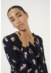 Navy blouse with long, puffed sleeves, featuring a floral pattern in pink and green. Ruffled neckline and elastic cuffs add texture.