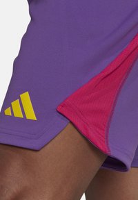Paarse sportshorts met roze accenten, gemaakt van een gladde stof, met een geel Adidas-logo en contrasterende stiksels.