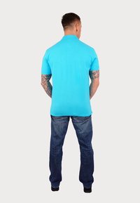 Ljusblå pikétröja med korta ärmar, i bomull, med ribbad krage och rak nederkant, tillsammans med mörkblå jeans.