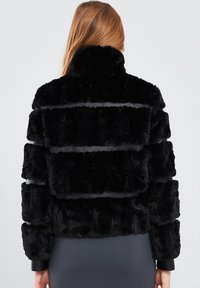 Black faux fur jacket with a textured, striped design and high collar. The sleeves are fitted, and the material appears soft and plush.
