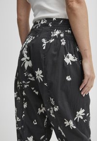 Czarne spodnie w kwiaty wykonane z lekkiego materiału, z elastycznym pasem i białym kwiatowym wzorem na całej powierzchni. Zbliżenie na tył i szczegóły kieszeni.