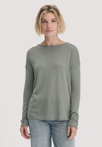 Langärmliger Pullover mit Rundhalsausschnitt aus weichem, hellgrünem Stoff. Hat eine lockere Passform mit ribbelten Ärmelbündchen und Saum. Kombiniert mit hellblauen Jeans.