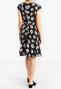 Czarna sukienka w kwiaty z krótkimi, odcinanymi rękawkami, ozdobiona różowymi i białymi kwiatami, z dopasowaną talią i rozkloszowanym dołem. Gładka tekstura materiału.