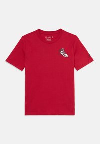T-shirt rouge à manches courtes avec un petit graphisme d'une basket rouge, blanche et noire sur la poitrine gauche et un petit logo sur la manche droite.