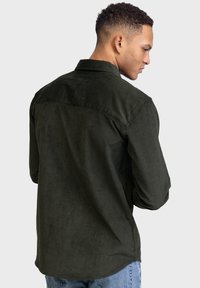 Donkergroene corduroy blouse met een zachte, gestructureerde afwerking, voorzien van een button-down kraag en een gebogen zoom. Zichtbare stikseldetails.