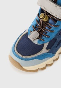 Baskets bleu et marine en daim et tissu, avec des lacets marron, un verrou en métal pour les lacets et une semelle en caoutchouc texturé.