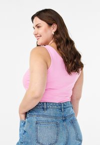 Vaaleanpunainen toppi, jossa on istuva muotoilu, yhdistettynä korkeavyötäröisiin farkkushortseihin. Ei tarranauhaa, sileä rakenne ja ei näkyviä kuvioita.