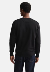 Zwarte sweatshirt gemaakt van zachte stof, met een ronde hals, geribbelde manchetten en een naadloos rugontwerp. Draagt blauwe spijkerbroek.