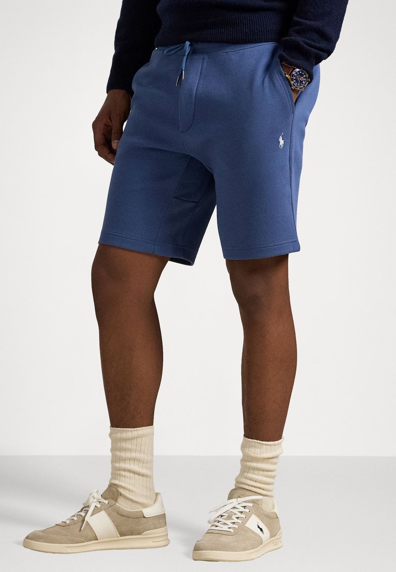 Shorts din bumbac albastru cu talie elastică și șnur de ajustare. Au buzunare laterale și un logo mic. Asortați cu adidași bej și șosete deschise.