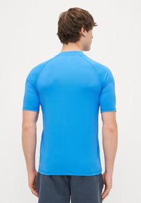 Īsām piedurknēm, sportisks piegriezums, krekls spilgti zils, izgatavots no gludas, elastīgas auduma. Iezīmē apaļu kakla izgriezumu un raglāna piedurknes.