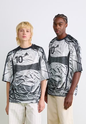 Twee volwassenen dragen bijpassende zwart-witte Adidas sportshirts met nummer 10, staande tegen een effen witte achtergrond.
