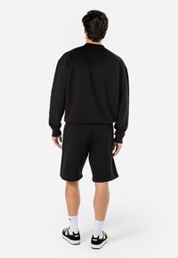 Tuta composta da felpa nera e pantaloni corti, realizzata in tessuto morbido. Caratterizzata da polsini a coste, vestibilità comoda e design minimalista. Indossata con sneakers.