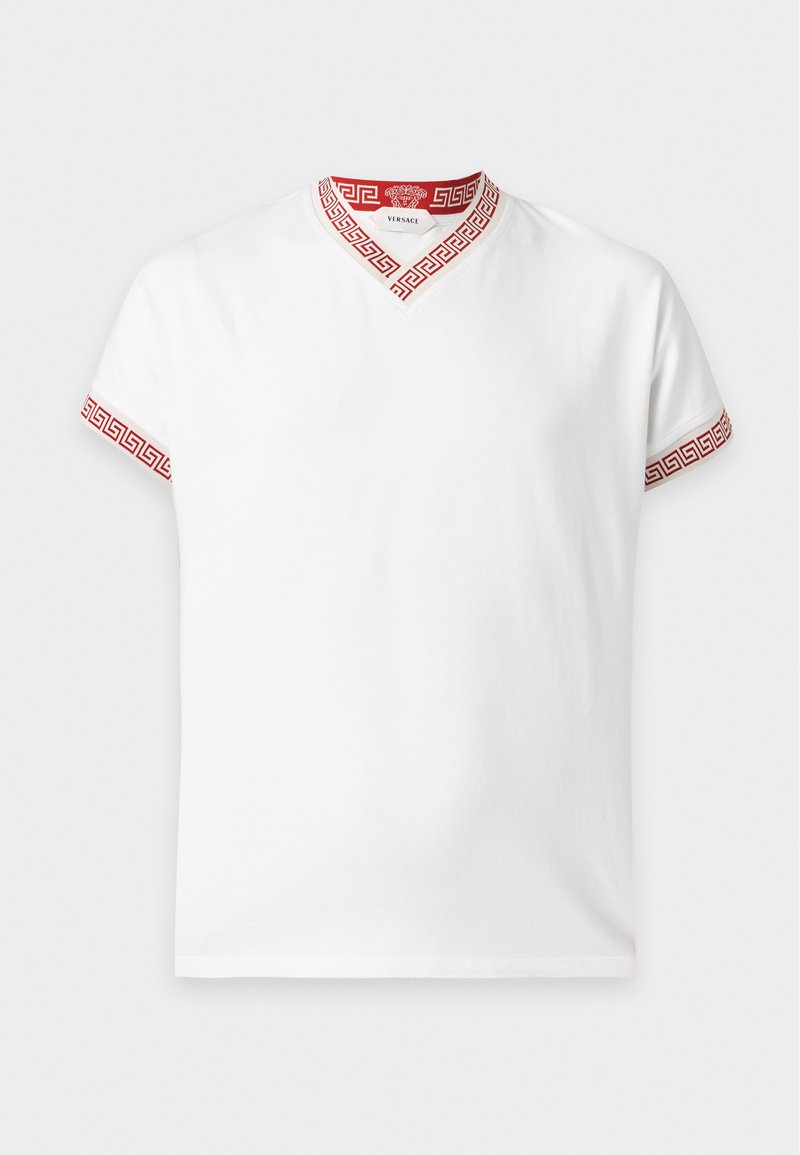 T-shirt blanc à manches courtes avec motif clé grecque rouge sur le col en V et les bords des manches, étiquette Versace à l'intérieur du col.