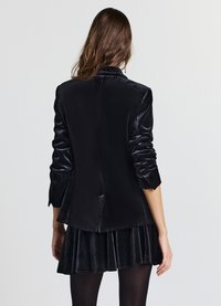 Schwarzer Samtblazer mit tailliertem Schnitt, langen Ärmeln und gepolsterten Schultern. Verfügt über einen einzelnen Rückenschlitz und eine glatte, glänzende Textur.