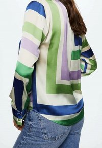 Blusa di seta con grandi motivi geometrici in viola, verde e blu. La camicia ha maniche lunghe e bottoni ai polsini, con una texture liscia.
