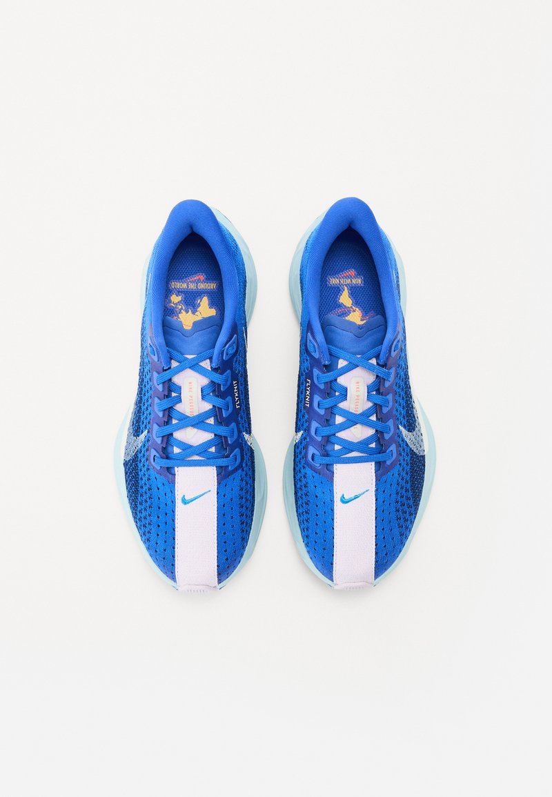 Zapatillas deportivas azules con parte superior de malla, suela exterior azul clara, detalles en blanco y rosa, y cordones azules. Presentan un prominente logo de Nike.