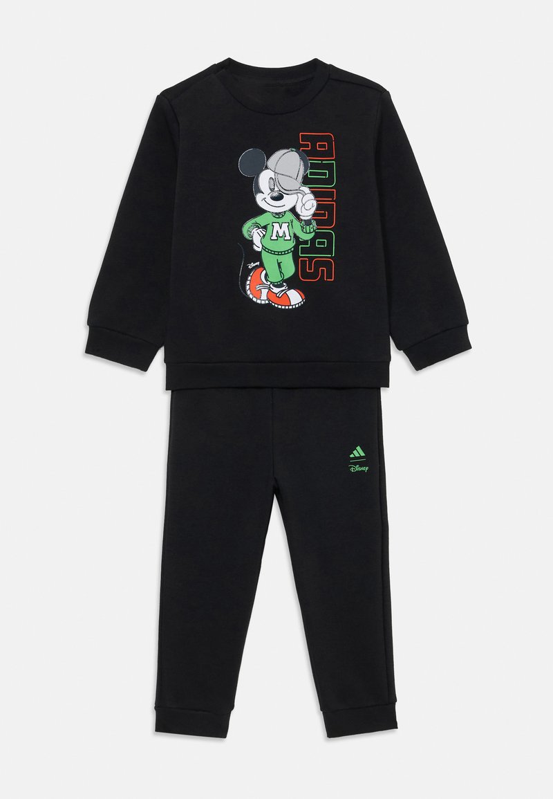 Melna divdaļīga treniņtērpa komplekts ar lielu Mickey Mouse grafiku augšdaļā, kurā ir redzams "Adidas" teksts krāsainās burtos.