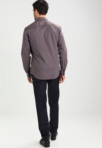 Camicia a maniche lunghe a quadri in marrone scuro e bianco, realizzata in cotone. Caratterizzata da un colletto, polsini con bottoni e orlo curvo. Abbinata a pantaloni blu navy.