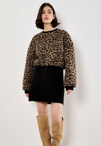 Pull en polaire à motif léopard avec une jupe noire à côtes, associé à des bottes en suède beige hauteur genou. Texture douce et design oversize.