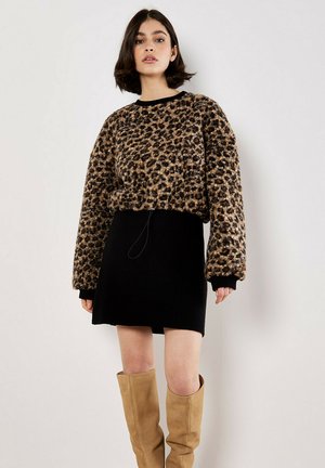 Pull en polaire à motif léopard avec une jupe noire à côtes, associé à des bottes en suède beige hauteur genou. Texture douce et design oversize.