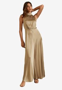 Beige halterneck jumpsuit med en figurnära bodice och lösa, flödande byxor. Slät, texturerad tyg och muddar med elastik.