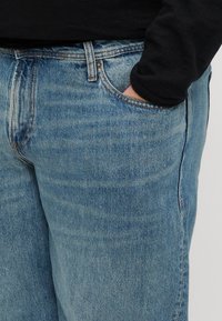 Jeans in denim azzurro chiaro con una vestibilità rilassata, dotati di cinque tasche, cuciture visibili e una leggera scoloritura per texture.
