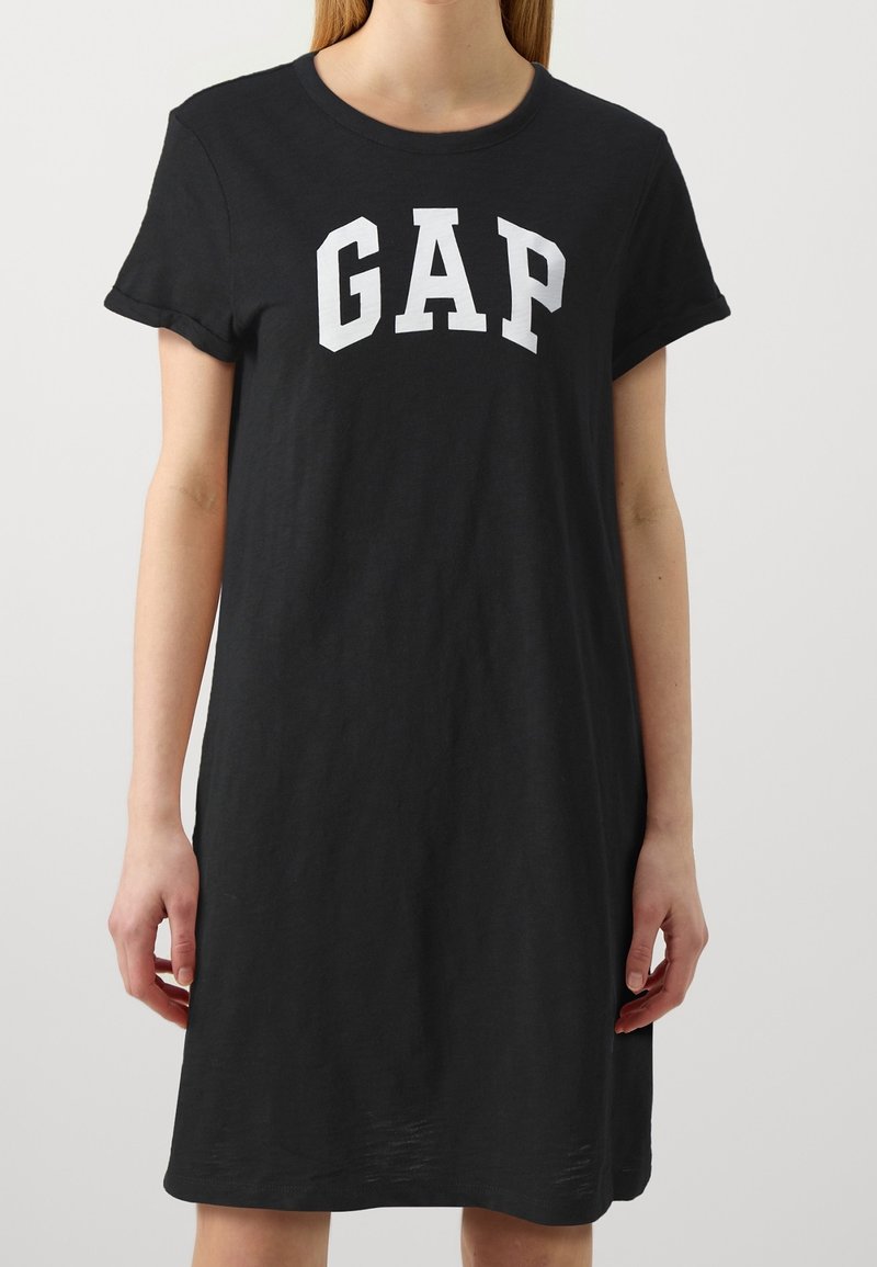 Černé bavlněné šaty ve tvaru trička s krátkými rukávy, kulatým výstřihem a bílým logem "GAP" napsaným tučným písmem napříč hrudí.