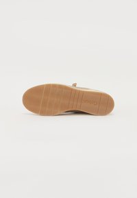 Suola delle scarpe in gomma marrone chiaro con scanalature a motivo evidenti per la trazione; parte superiore morbida beige e linguetta sul tallone per una facile calzata.