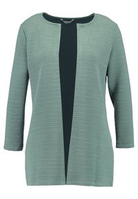 Texturerad ljusgrön tunika med trekvartsärmar, rund halsringning och en mörk mittpanel. Vertikalt ribbat mönster framhäver designen.