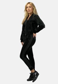 Czarny dres z weluru z kurtką bomberką na zamek i dopasowanymi spodniami z bocznymi paskami. Uzupełniony czarnymi trampkami za kostkę.