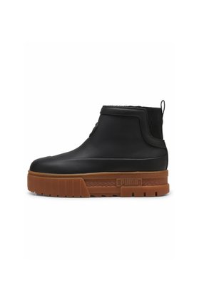 Zwarte enkelboot met een gestructureerde zwarte elastische zijkant, bruine chunky zool en logo-detail, gemaakt van rubber en heeft een modern ontwerp.