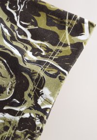 Țesătură de bumbac cu un model camuflaj în verde închis, negru și alb. Prezintă cusături drepte de-a lungul marginii. Finisaj texturat.