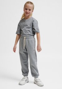 Grijze katoenen T-shirt en bijpassende grijze joggingbroek met elastische boorden. Heeft een subtiel ontwerp op de borst. Afgemaakt met witte sneakers.