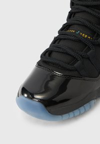 Μαύρο αθλητικό παπούτσι με στιλπνό δερμάτινο περίβλημα δακτύλων, υφασμάτινο επάνω μέρος με υφή και πλεκτά κορδόνια. Διαθέτει διαφανές, παγωμένο μπλε εξωτερικό πέλμα.